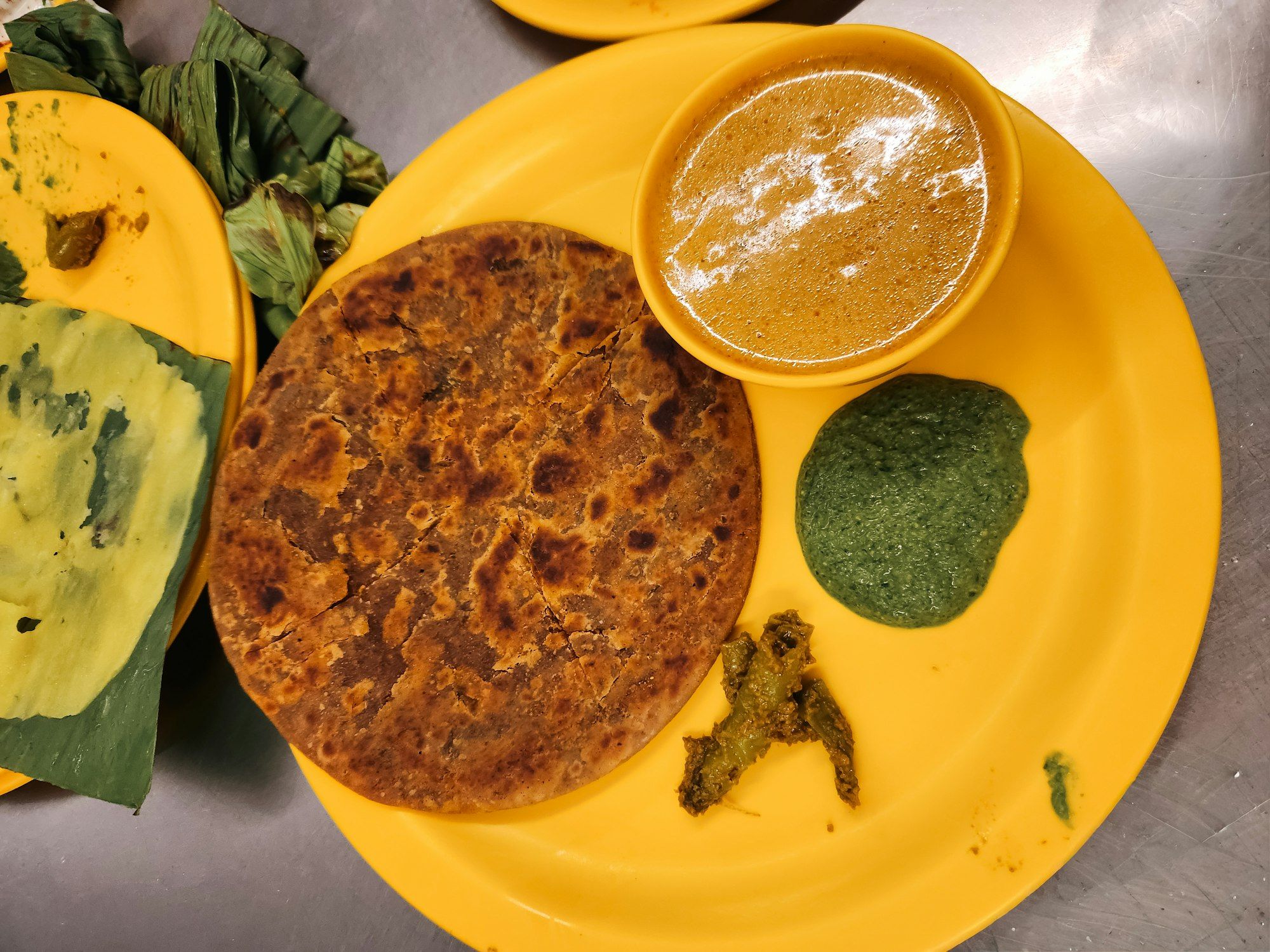 A home breakfast of flaky parathas with a bowl of curry, green chutney and pickle.