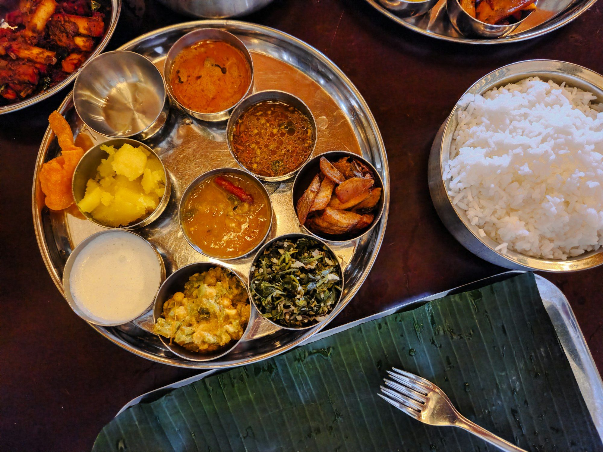 A vegetarian thali in steel bowls: dal, vegetables, curd and rice on a round steel plate.