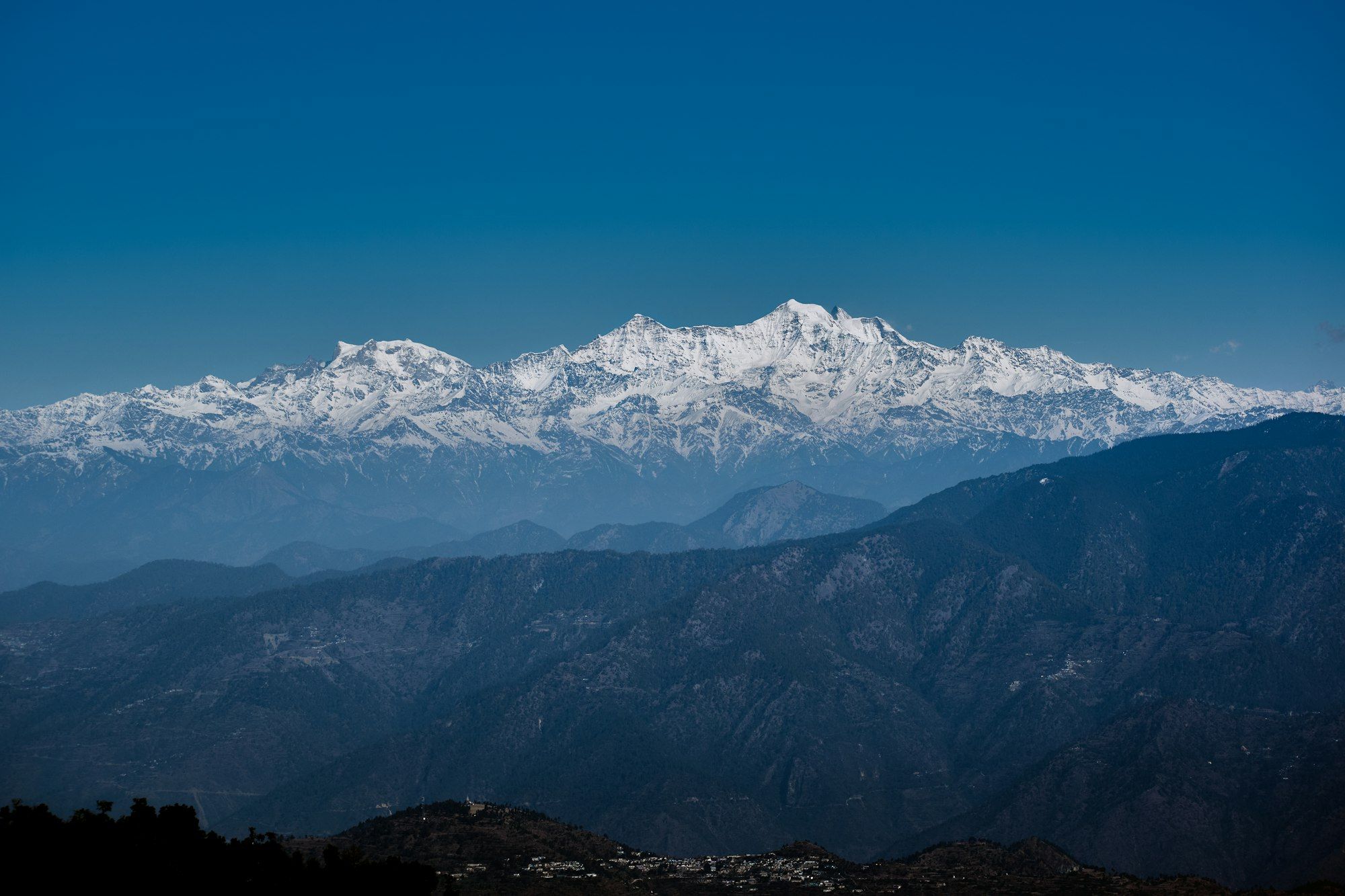 A long line of Himalayan snow peaks above layers of blue hills in the morning.